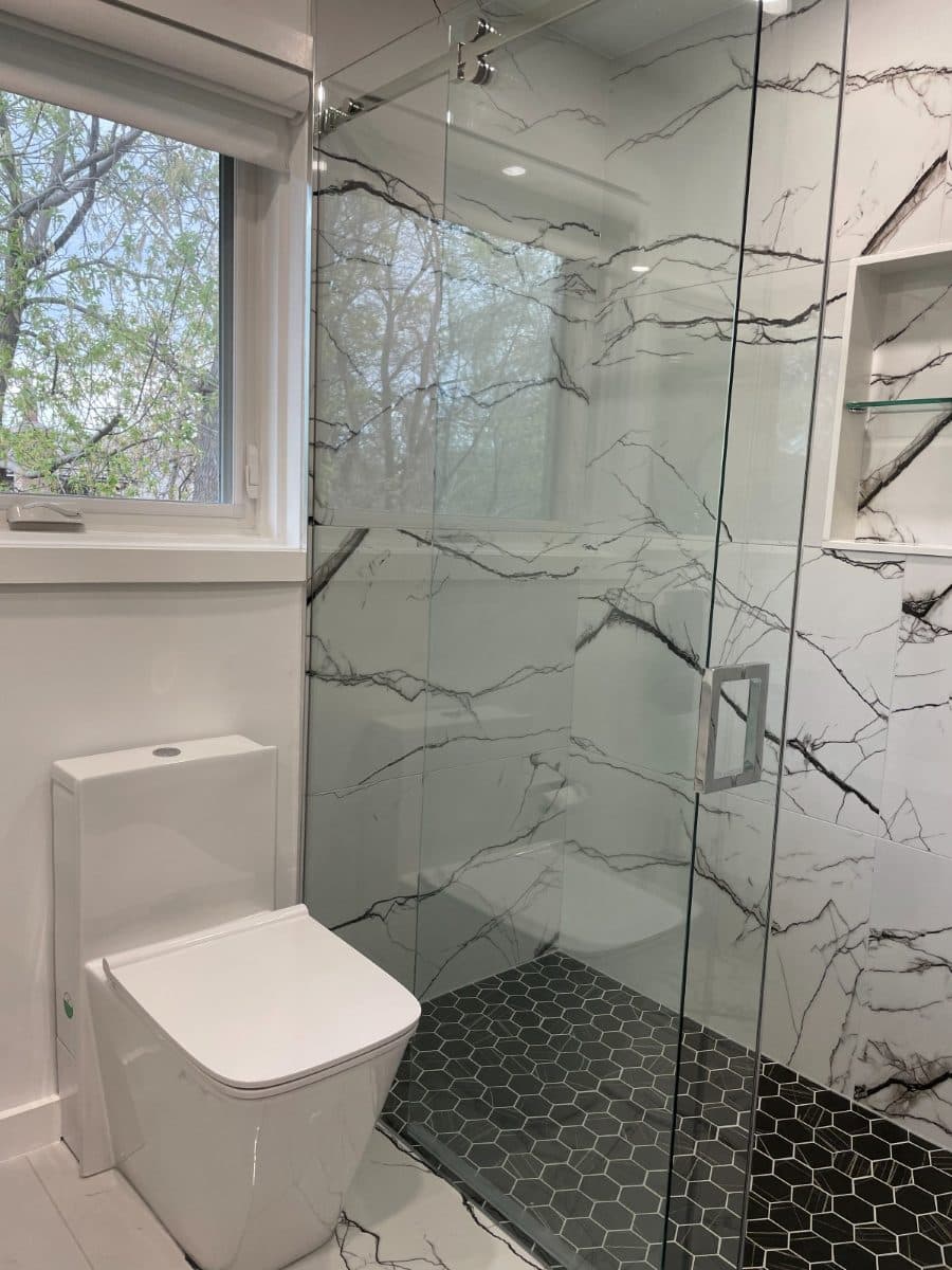 Finished bathroom with a wall-hung toilet and glass shower enclosure against marble tiling.