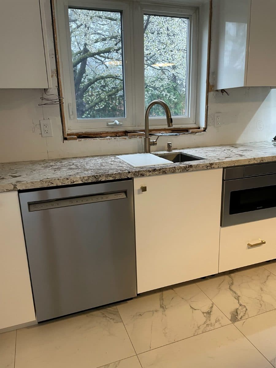 Stainless dishwasher fitted under a marble worktop beside an undermount sink.