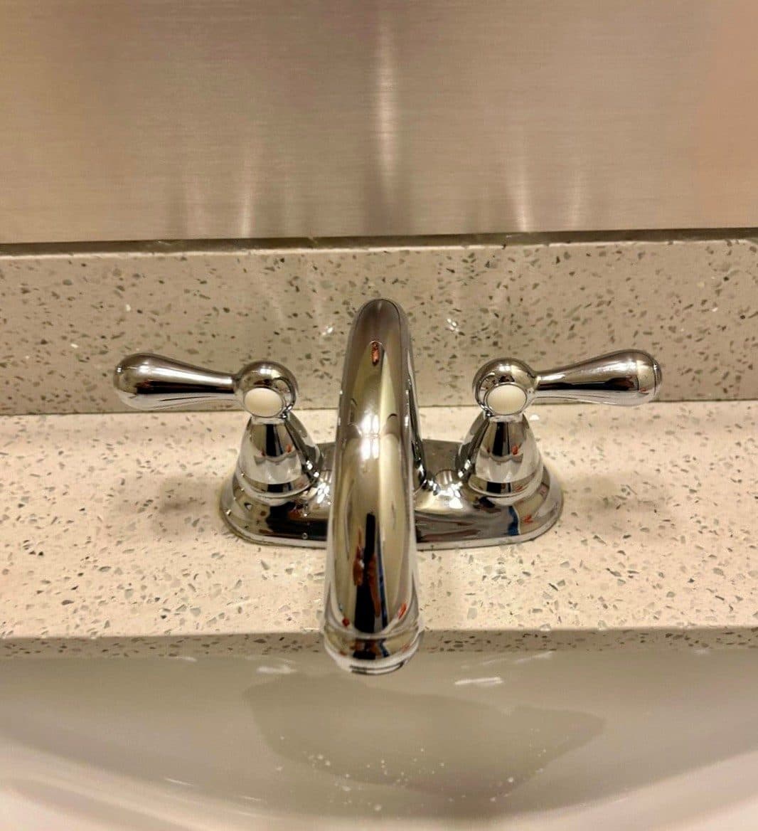 Polished chrome two-handle basin mixer fitted to a speckled quartz vanity top.