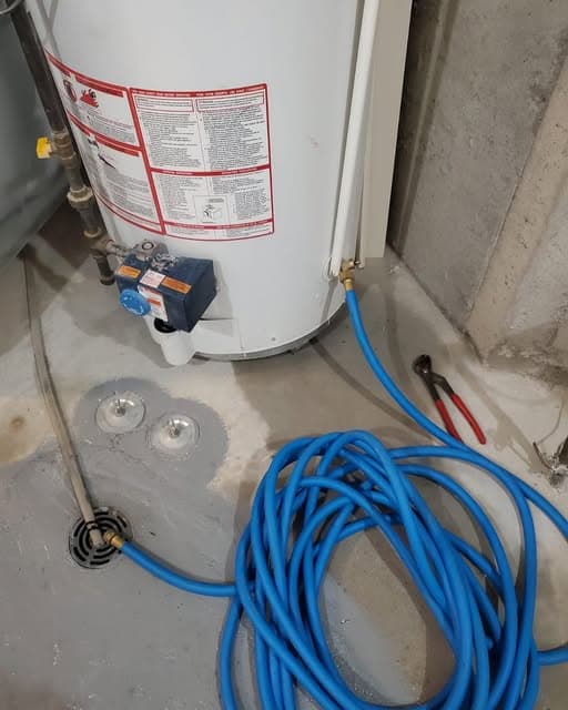 Hot water tank in a basement with blue PEX supply line coiled and connected to a floor drain.