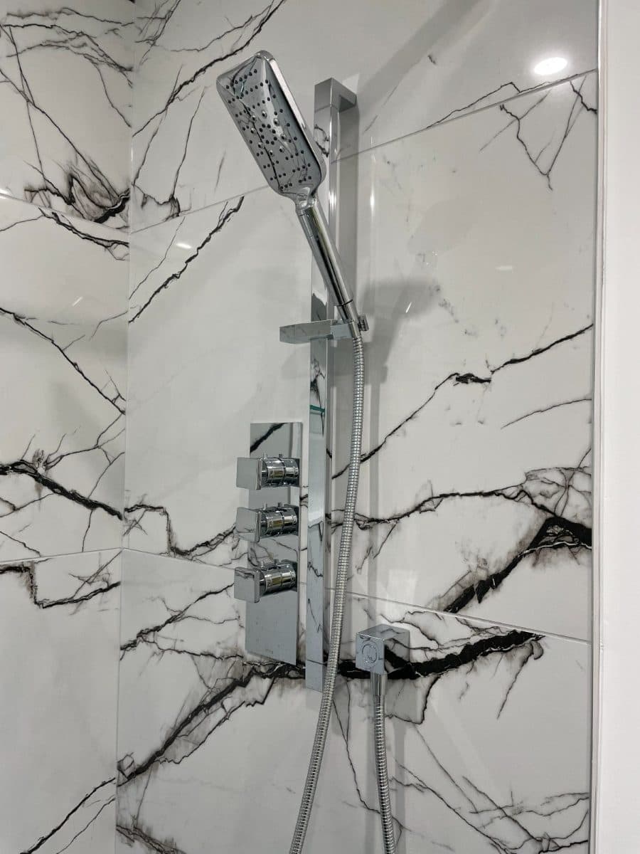 Walk-in shower with a rain head, handheld and thermostatic valve set into a marble wall.