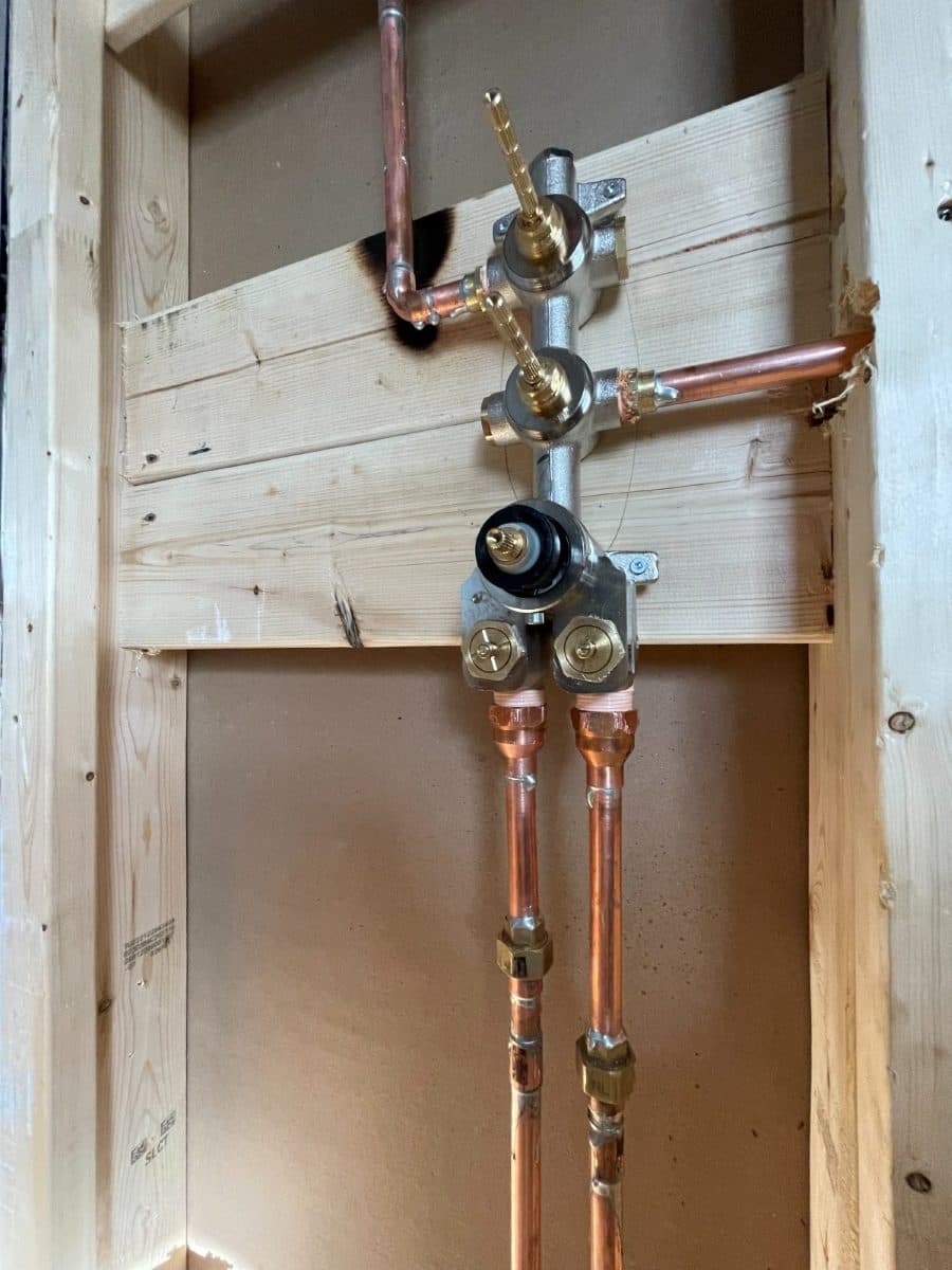 Copper supply lines and shower valve roughed into an open stud wall before drywall.
